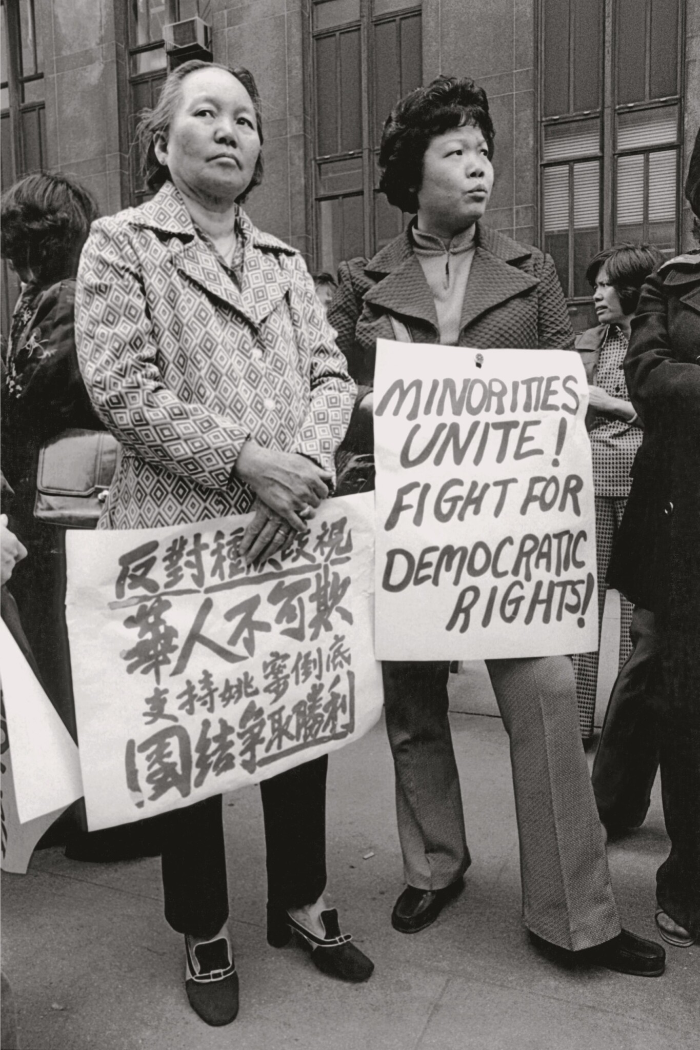 Two Asian American women hold signs in English and Chinese writing, in black and white.