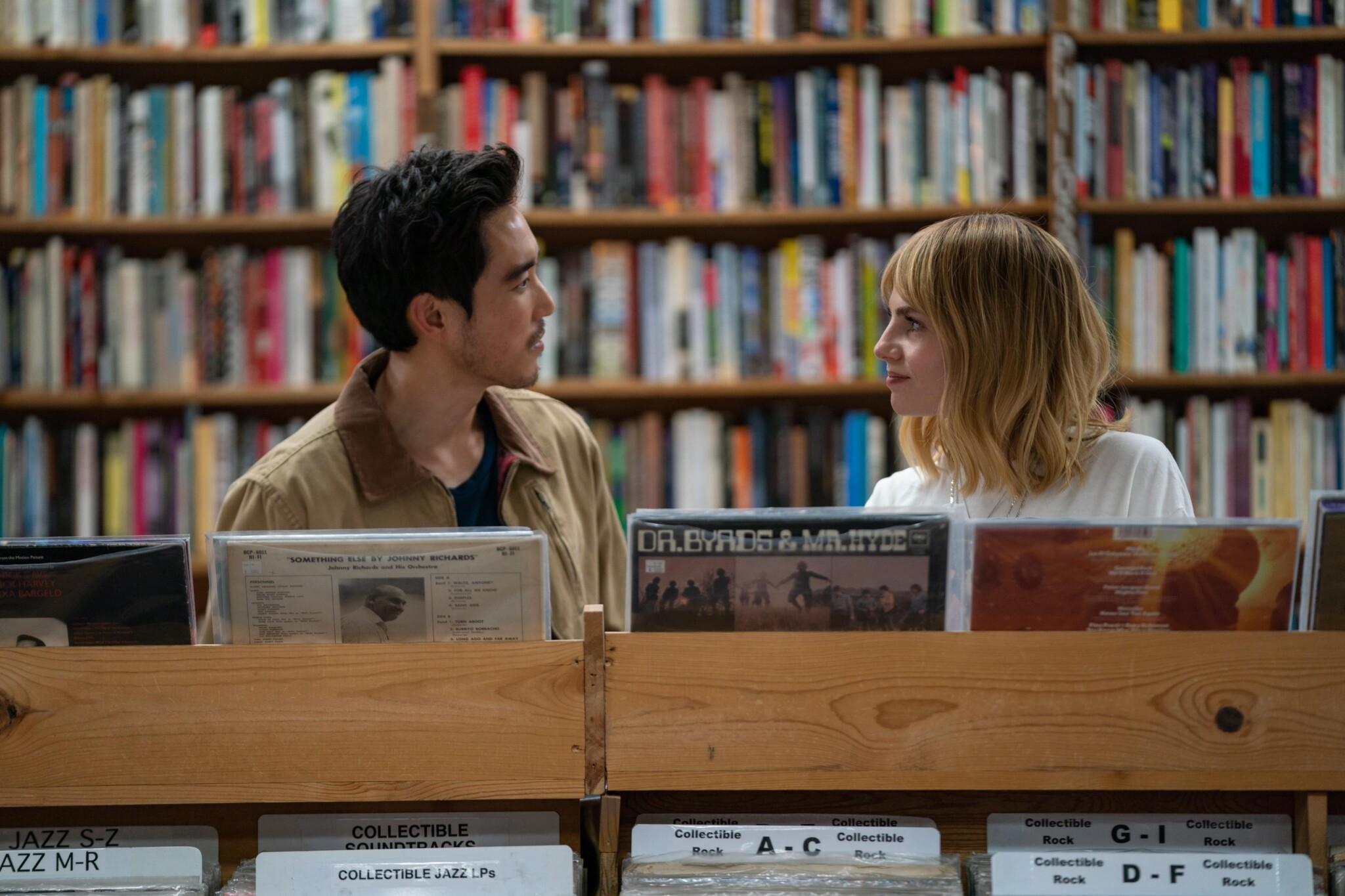 Justin H. Min and Lucy Boynton in "The Greatest Hits" stand looking at each other in a record shop.