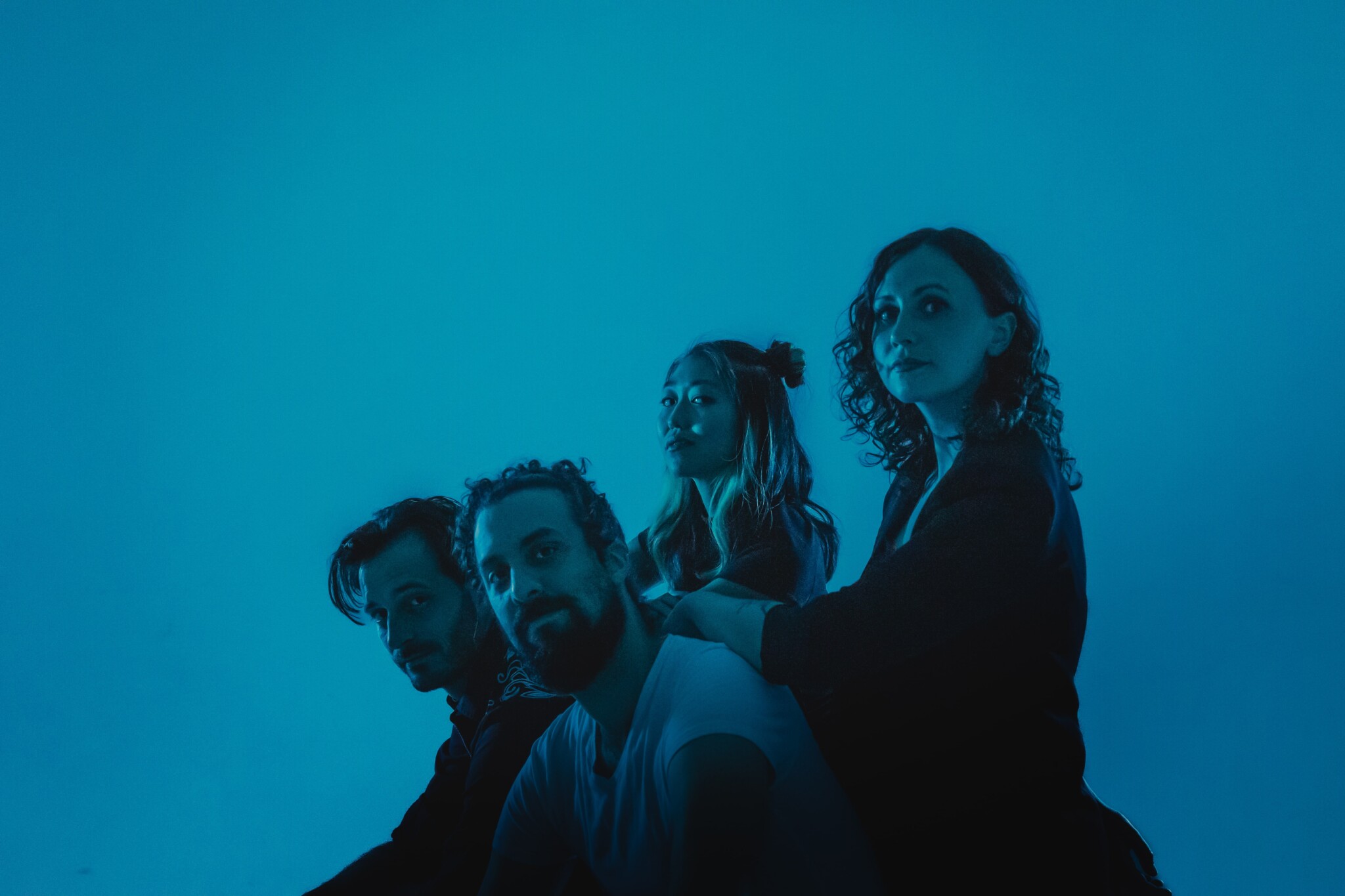Four people look towards the camera with their bodies facing to the left under blue lighting.