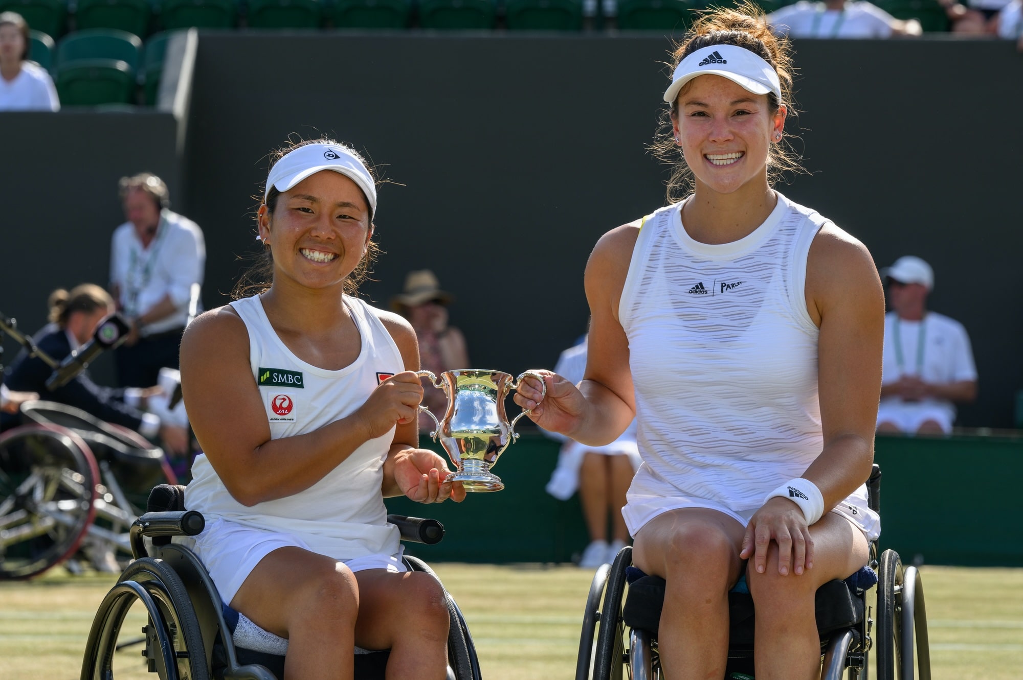 Japanese wheelchair tennis player Yui Kamiji and American wheelchair tennis player Dana Mathewson, in white, hold a trophy together at Wimbledon.
