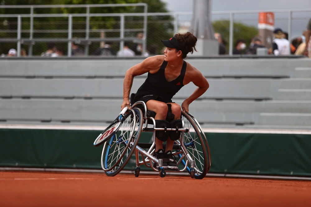 Wheelchair tennis player Dana Mathewson dressed in black sits on a clay court, holding a racket.