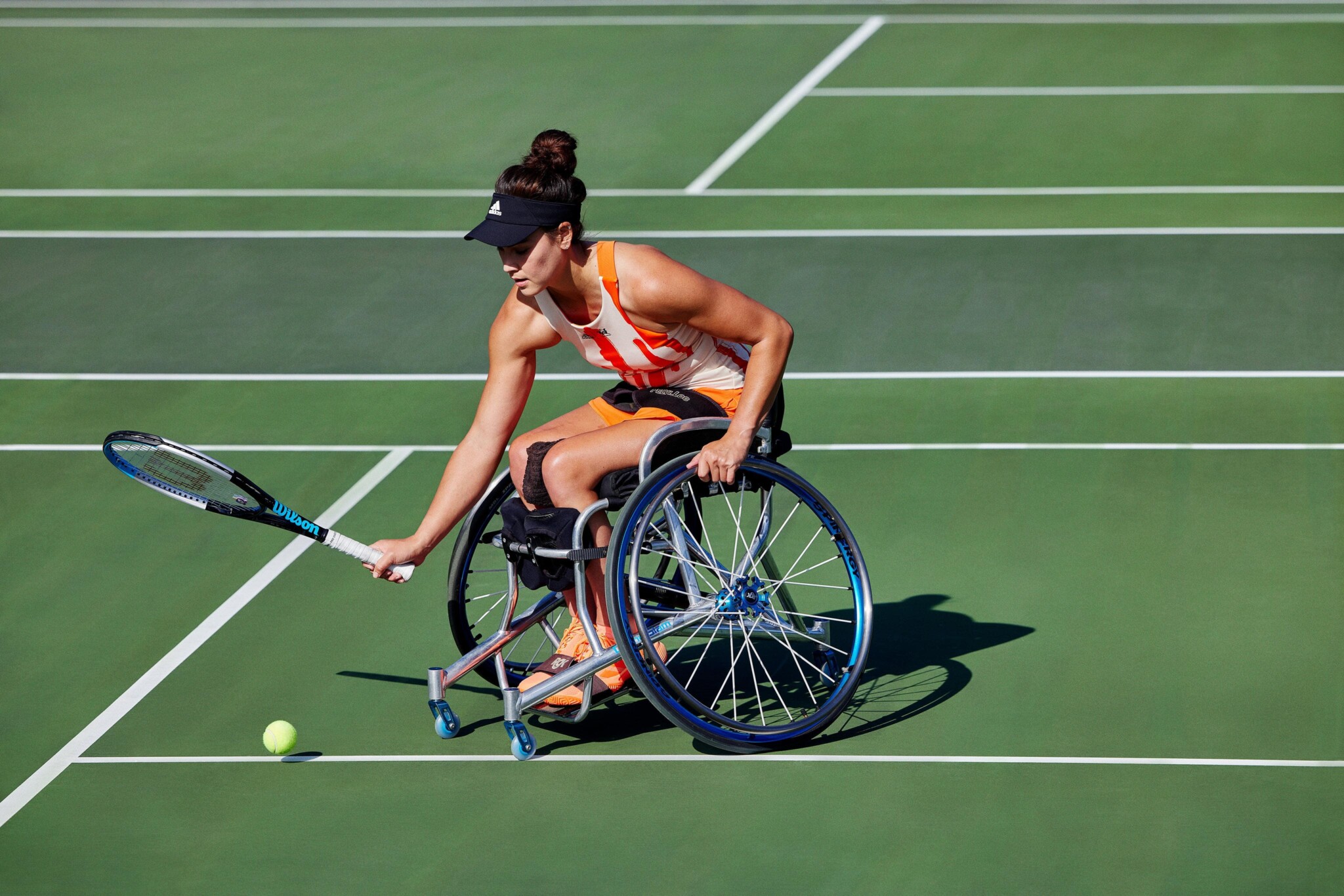Wheelchair tennis player Dana Mathewson sits in her char with a racket stretched out to hit a tennis ball.